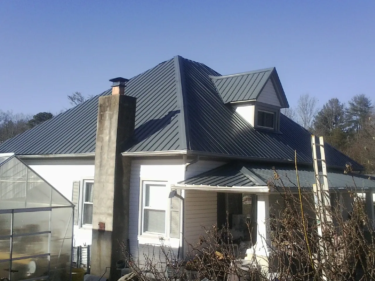 Dark blue standing seam metal roof on a white farmhouse with dormer — Slate & Tile Roof Repair by Roofing Brothers in Powellsville