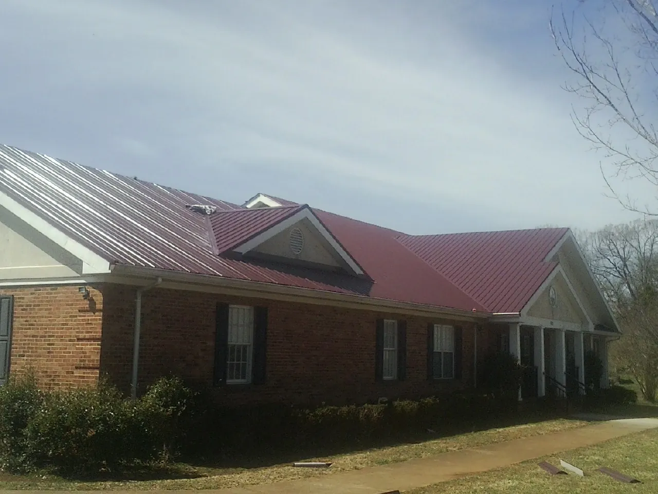 Red metal roof with gabled entries on a long brick building, from a Hail Damage Roof Repair job in Powellsville