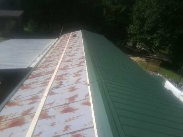 Old rusted panels beside newly installed green metal roofing — Wind Damage Roof Repair by Roofing Brothers in Powellsville
