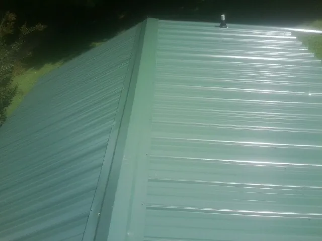 New green metal panels meeting at the ridge of a roof — Flat Roof Repair work by our crew in Powellsville