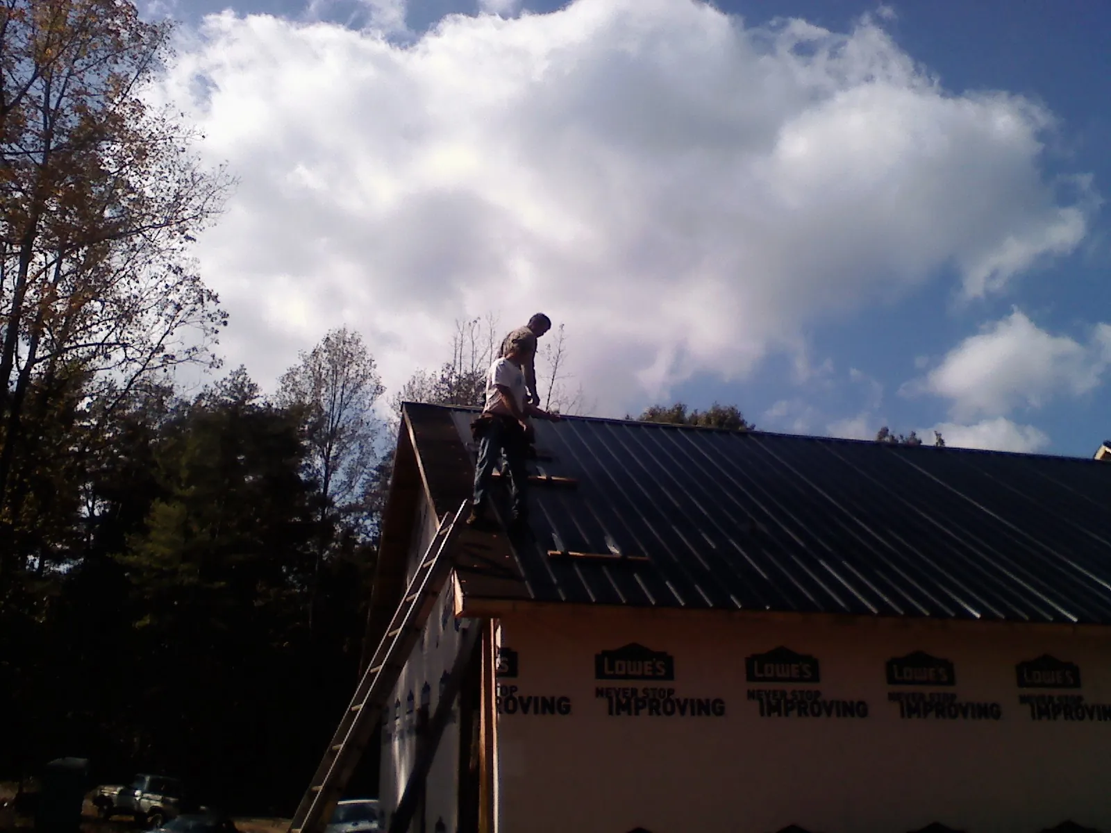 Roofer fastening dark metal panels high against a cloudy sky, from a Roof Inspection job in Powellsville