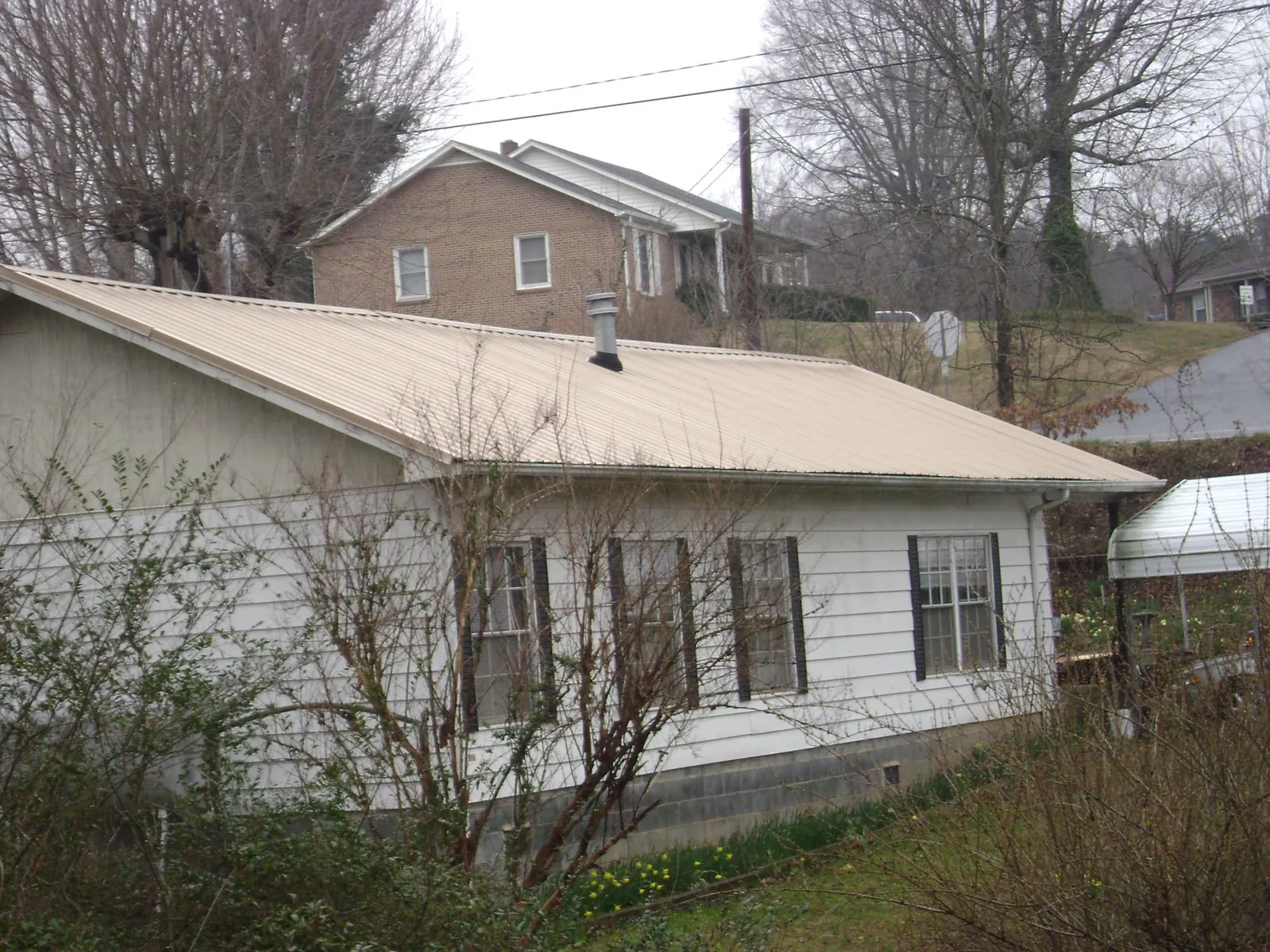Tan metal roof on a white sided house set into a hillside — Commercial Roofing by Roofing Brothers in Powellsville