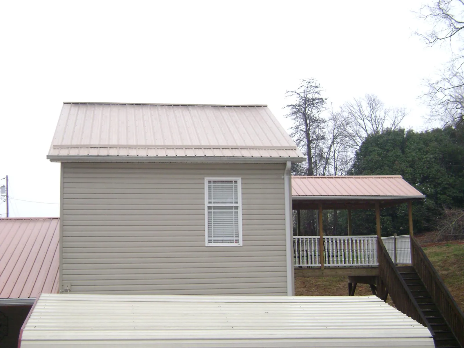 Tan metal roofs on a two story addition and attached porch, from a Roof Replacement job in Powellsville